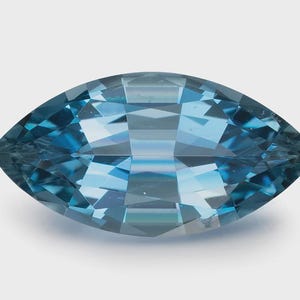 Può includere: Una pietra preziosa taglio marquise di colore blu intenso con una superficie sfaccettata. La pietra presenta una forma ovale appuntita con tagli geometrici simmetrici che riflettono la luce, creando un aspetto chiaro e levigato.