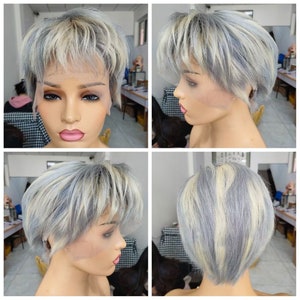 May include: A short, gray and blonde wig with a side part. The wig is styled in a pixie cut with bangs.