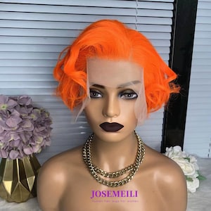 May include: A short, bright orange wig with a wavy style. The wig is on a mannequin head with a gold chain necklace. The text "JOSE MEILI human hair wigs for women" is at the bottom of the image.