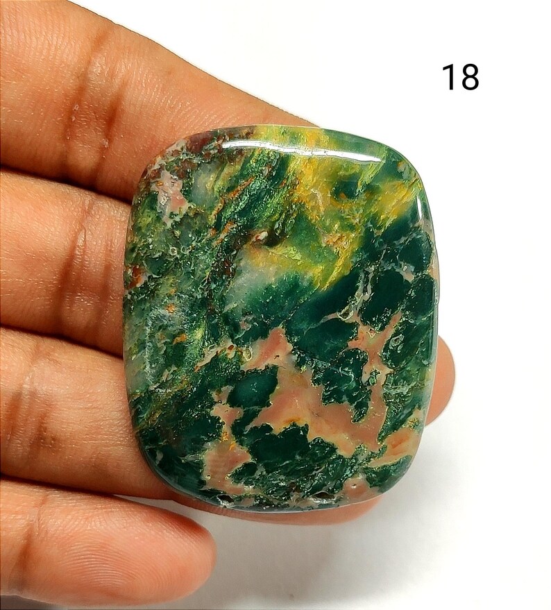 May include: A polished, rectangular-shaped gemstone with rounded corners, featuring a marbled pattern of deep forest green, vibrant yellow, and soft peach-colored inclusions. The stone has a smooth, glossy surface and is marked with the number 18.