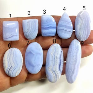 Pode incluir: Nove pedras preciosas de ágata azul rendada polidas em várias formas, incluindo retangular, gota e oval. Cada pedra exibe um padrão único de faixas azuis claras e brancas, mostrando variações naturais.