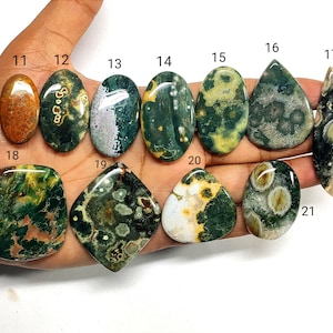 May include: A collection of eleven polished, multi-colored ocean jasper cabochons labeled with numbers 11 through 21. The stones feature various shapes including oval, teardrop, diamond, and irregular forms with green, yellow, and brown patterns.