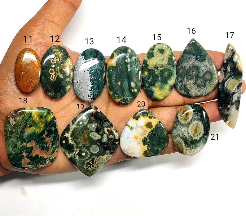 May include: A collection of eleven polished, multi-colored ocean jasper cabochons labeled with numbers 11 through 21. The stones feature various shapes including oval, teardrop, diamond, and irregular forms with green, yellow, and brown patterns.