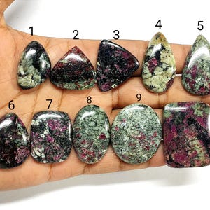 May include: Ten polished cabochon gemstones labeled 1 through 10, featuring a mix of deep red, black, and light green mineral inclusions. Each stone has a smooth, glossy surface and unique, irregular patterns of color throughout the material.