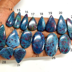 May include: A collection of polished, teardrop and oval-shaped gemstones featuring a mottled blue and magenta color pattern. Each stone is individually numbered from 14 to 29, showcasing a smooth, reflective surface with distinct mineral inclusions.