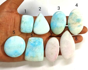 Peut inclure: Un assortiment de huit pierres précieuses polies de formes variées. Les pierres présentent une gamme de couleurs, notamment le bleu clair, le blanc et le rose. Les pierres sont tenues dans une main, mettant en valeur leurs caractéristiques et textures individuelles. La collection comprend des formes ovales, en goutte et rectangulaires.