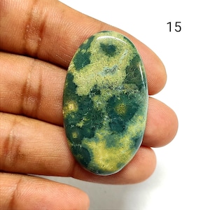 May include: An oval-shaped polished gemstone cabochon featuring a mottled pattern of deep forest green and pale yellow inclusions. The stone has a smooth, reflective surface and is marked with the number 15 in the upper right corner.