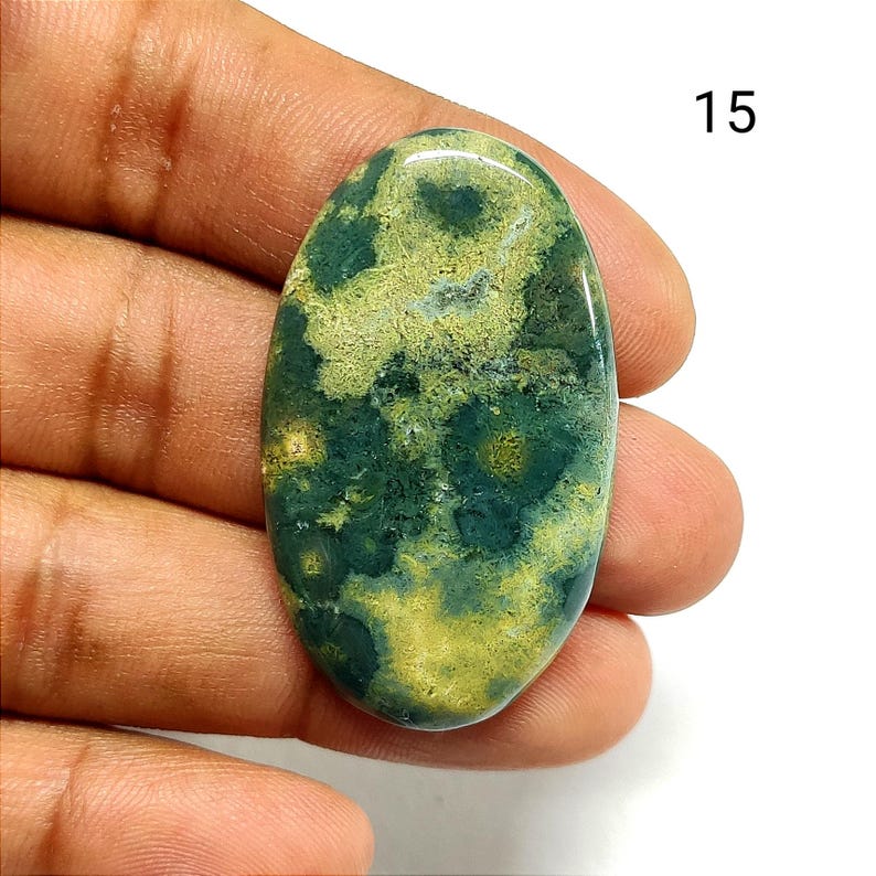 May include: An oval-shaped polished gemstone cabochon featuring a mottled pattern of deep forest green and pale yellow inclusions. The stone has a smooth, reflective surface and is marked with the number 15 in the upper right corner.