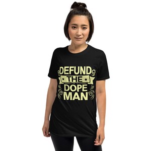 Peut inclure: T-shirt noir avec un graphisme jaune qui dit "DEFUND THE DOPE MAN" dans un design de banni&egrave;re.