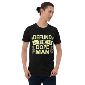 Peut inclure: T-shirt noir avec un motif jaune qui dit "DEFUND THE DOPE MAN" avec des &eacute;toiles et des volutes autour du texte.