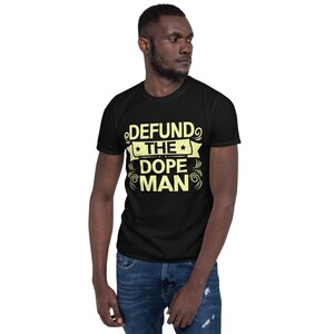 Peut inclure: Un t-shirt noir avec un motif jaune qui dit "DEFUND THE DOPE MAN" dans une police de caract&egrave;res stylis&eacute;e.