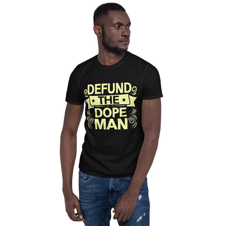 Peut inclure: Un t-shirt noir avec un motif jaune qui dit "DEFUND THE DOPE MAN" dans une police de caract&egrave;res stylis&eacute;e.