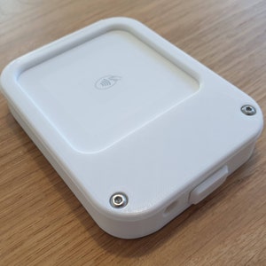 May include: White plastic square-shaped card reader with a logo and two screws on the side.