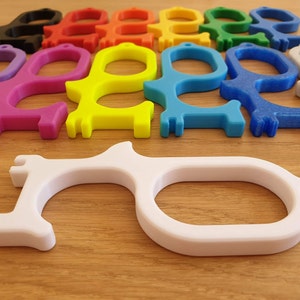 May include: A collection of colourful door openers, also known as touch tools, made of plastic. The tools are designed to help people avoid touching surfaces in public places. The tools are in a variety of colours, including purple, pink, yellow, blue, and white.