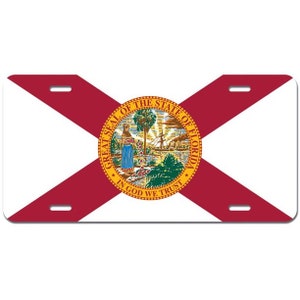 May include: A red and white Florida state flag license plate with the state seal featuring a woman standing next to a tree and a ship. The seal is surrounded by the words "Great Seal of the State of Florida" and "In God We Trust".