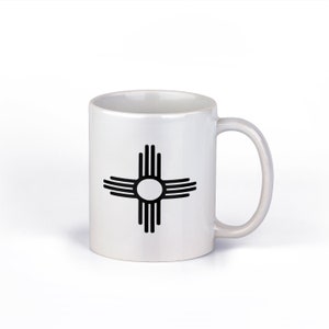 May include: White ceramic mug with a black Zia symbol, a traditional symbol of the Pueblo people of New Mexico.