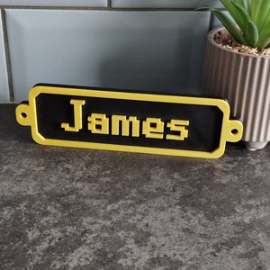 May include: A black and yellow nameplate with the name "James" in pixelated letters.