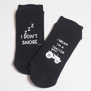 May include: A pair of black socks with white text. One sock says "zzz I don't snore..." and the other sock says "I dream I'm a tractor" with a small tractor graphic.