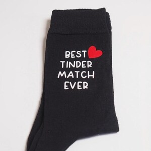 May include: Black socks with white text that reads "Best Tinder Match Ever" and a red heart.