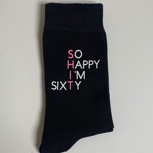 May include: Black socks with white text that reads "SO HAPPY I'M SIXTY" with the "I" in pink.