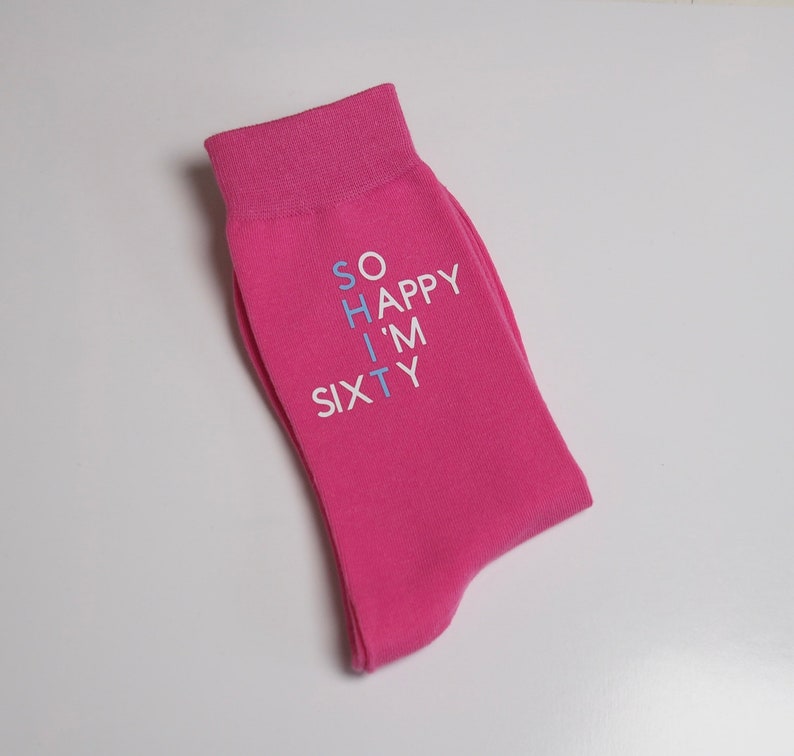 May include: Pink socks with the text "SO HAPPY I'M SIXTY" written in white and blue.