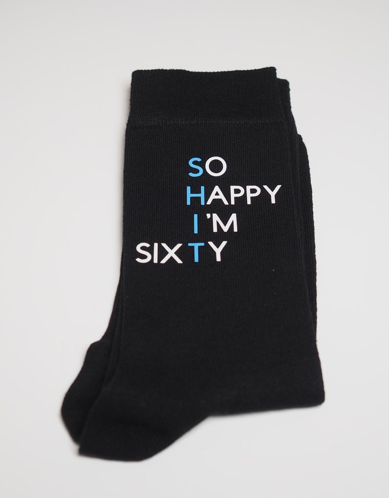 May include: Black socks with white text that reads "SO HAPPY I'M SIXTY" in blue and white lettering.