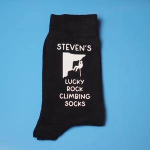 May include: Black socks with a white graphic of a person rock climbing with the text "STEVEN'S LUCKY ROCK CLIMBING SOCKS"