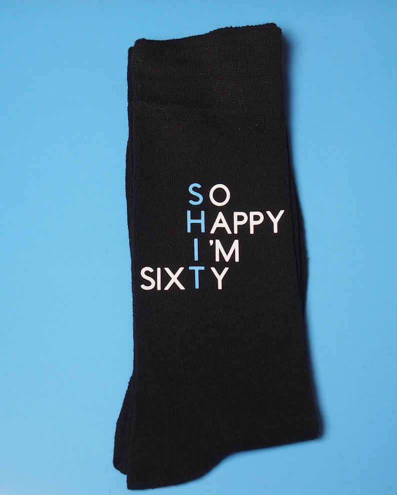 May include: Black socks with white text that reads "SO HAPPY I'M SIXTY". The word "I'M" is in blue.