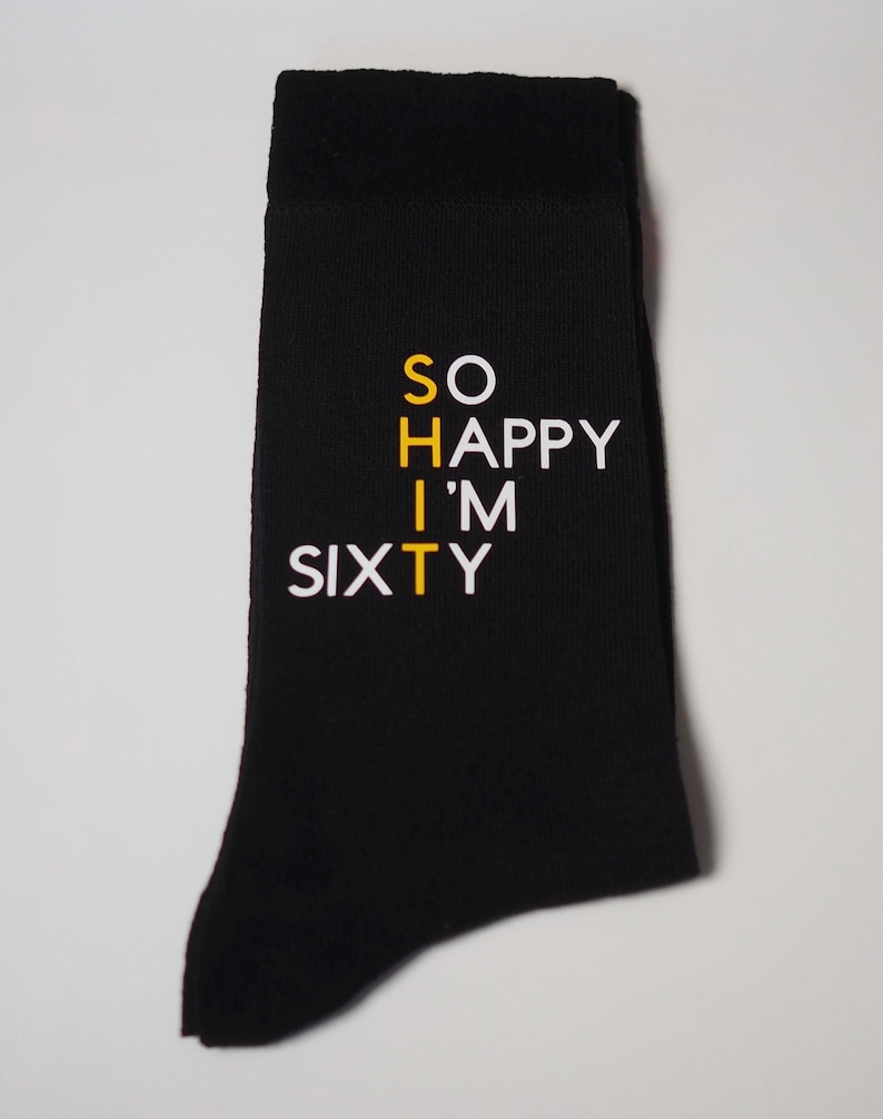 May include: Black socks with white text that reads "SO HAPPY I'M SIXTY" with the "T" in "SIXTY" in yellow.