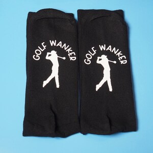 May include: A pair of black socks with a white silhouette of a golfer and the text "GOLF WANKER" printed on each sock.