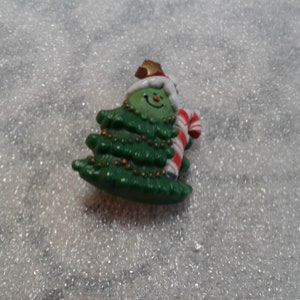 May include: A green Christmas tree ornament with a smiling face, wearing a white hat and holding a candy cane.