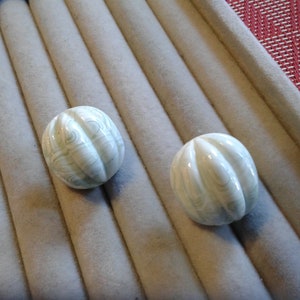 Puede incluir: Dos botones de cerámica blanca con un patrón de espiral. Los botones son redondos y tienen un diseño ligeramente elevado.