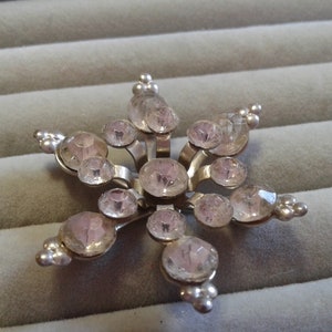 May include: A silver snowflake brooch with clear pink rhinestones.