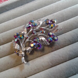 May include: A silver brooch with a floral design featuring iridescent red, purple, and blue rhinestones.