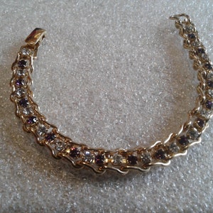 May include: A gold chain bracelet with alternating clear and purple rhinestones.