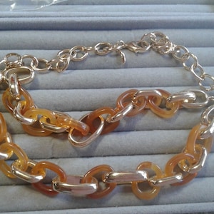 May include: A gold chain necklace with large, amber-colored links. The chain is layered on top of itself, creating a thick, chunky look.