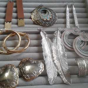 May include: Assortment of silver and gold tone earrings, including hoop earrings, feather earrings, and circular earrings with turquoise and pink accents. Also included are two silver heart-shaped earrings and two silver cuff bracelets.