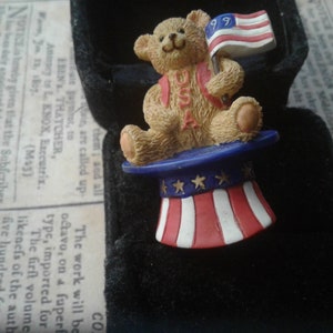 Avon giethars patriottische teddybeerspeld, gedateerd '99, met Amerikaanse vlag, zittend in met sterren versierde hoge hoed, gemarkeerd met VS op buik