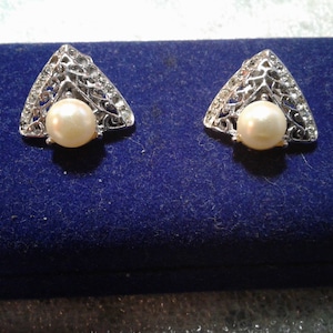 May include: A pair of silver earrings with a triangular design and a white pearl in the center of each earring.