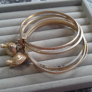 Puede incluir: Cuatro pulseras de brazalete doradas con un patrón grabado decorativo. Las pulseras tienen dos pequeños abalorios redondos dorados.