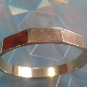 Könnte beinhalten: Ein goldfarbenes Armreif-Armband mit sechseckiger Form. Das Armband ist glatt und glänzend.