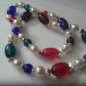 May include: A multi-colored beaded necklace with white, red, blue, green, and purple beads. The necklace is made of glass and pearl beads.