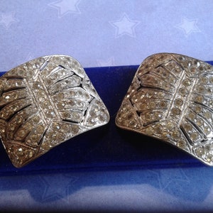 May include: A pair of silver-toned shoe buckles with a geometric design, featuring a large number of clear rhinestones.