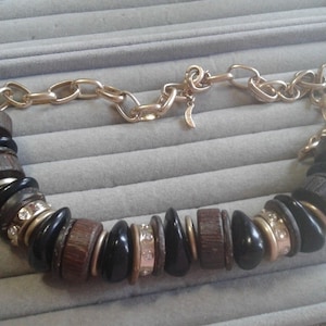 May include: A gold chain necklace with wooden and black beads, some of which are accented with rhinestones.