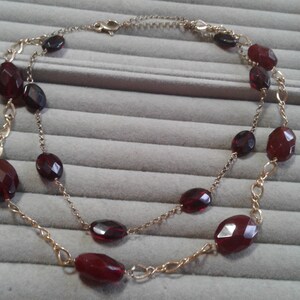 May include: A gold chain necklace with a double strand of red gemstone beads. The beads are oval shaped and have a faceted finish.