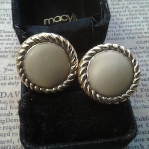 May include: A pair of gold-tone earrings with white pearl-like stones set in a rope-like design. The earrings are in a black velvet box with the Macy's logo.