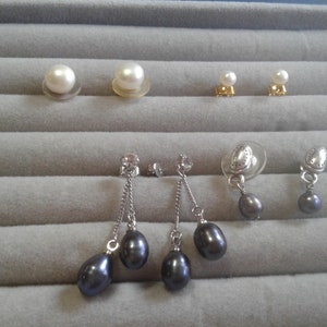 May include: A set of pearl earrings, including a pair of white pearl stud earrings, a pair of white pearl drop earrings, and a pair of black pearl drop earrings.