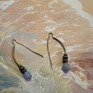 May include: A pair of silver earrings with a light blue agate bead on each. The earrings are made of wire and have a simple design.