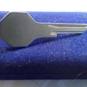Puede incluir: Una llave plateada con una cabeza octogonal única y un solo corte en el eje. La llave está sobre una superficie de terciopelo azul.