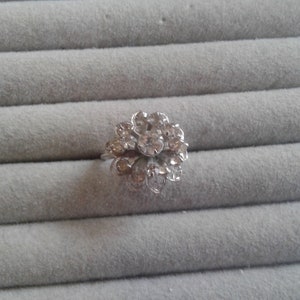 Puede incluir: Un anillo de plata con un diseño de flor con diamantes de imitación transparentes.